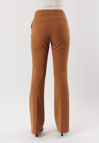 Pantaloni marroni a campana realizzati in tessuto morbido. Presentano una vita alta, due tasche posteriori e una vestibilità sartoriale attraverso le cosce.