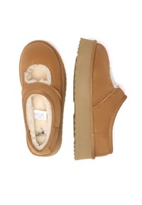 Brown slip-on shoes with a soft, textured exterior and plush lining. Rounded toe and thick, ridged sole. Cutout design at the front.