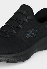 Μαύρο αθλητικό παπούτσι Skechers με ελαστικά κορδόνια τύπου bungee, υφασμάτινο πλεκτό με υφή, επενδεδυμένη σόλα και ανακλαστικό λογότυπο Skechers "S" στο πλάι.