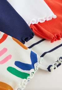 Gros plan des bords de tissu côtelés avec des ourlets à volants en bleu marine uni, blanc, rouge et blanc avec des formes abstraites multicolores et des rayures.