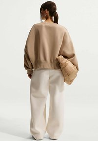 Μπεζ φαρδιά φούτερ με μακριά μανίκια και ριμπ τελείωμα, σε συνδυασμό με φαρδιά λευκά παντελόνια και μια ταμπά φουσκωτή τσάντα.