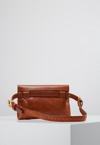 Borsa a tracolla in pelle marrone con pattina pieghevole, caratterizzata da una tracolla testurizzata decorata con shape a piramide e dettagli in metallo dorato.