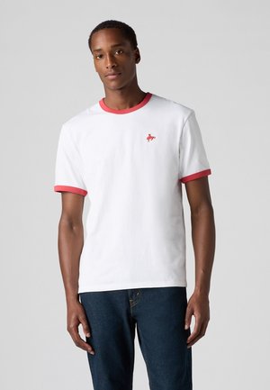 White t-shirt with red ribbed collar and sleeves, featuring a small red logo on the left chest. Soft cotton material, casual fit.