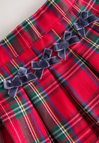 Röd plisserad kjol i rutig design med gröna, gula och svarta ränder; dekorerad med tre mörkblå sammetsrosetter vid midjan; veckad design.