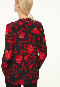 Maglietta nera con grande motivo floreale rosso, maniche lunghe, orlo arrotondato e tessuto leggero. Leggero lucido aggiunge texture al design.