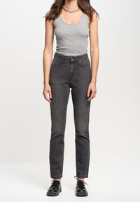 Débardeur gris et jeans noirs taille haute à coupe ajustée. Des chaussures noires à lacets complètent la tenue. Design simple et fonctionnel.