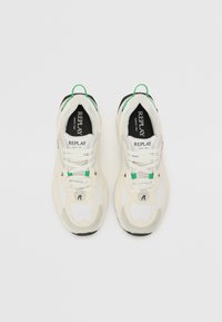 Sneakers bianche con materiale in rete e sintetico, dettagli verdi e neri, collare imbottito e suola testurizzata. Logo visibile sulla linguetta.