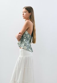 Top peplum de patrón floral en verde y crema con una cintura fruncida, combinado con una falda maxi blanca con volantes. Texturas suaves en toda la prenda.