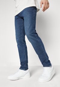 Vaqueros de mezclilla azul con corte ajustado, que presentan una textura suave y un ligero desgastado, combinados con zapatillas deportivas blancas.