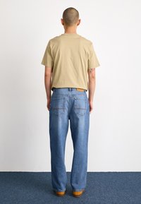 Beige short-sleeve T-shirt paired with light blue wide-leg jeans featuring double back pockets. The outfit is completed with brown shoes.