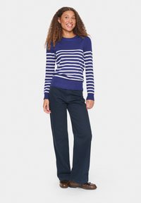 Pull rayé bleu marine et blanc avec un col rond, des poignets et un ourlet côtelés. Associé à un pantalon bleu marine ample et des chaussures marron.