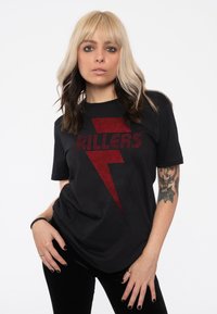 Black t-shirt featuring red lightning bolt design with the word "KILLERS" in a bold, pixelated font. Short sleeves and soft fabric.