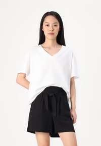 Vitt V-ringat t-shirt i mjukt tyg, kombinerat med högmidjade svarta shorts med en rosettdetalj vid midjan.