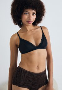Zwarte bralette met kant en hoge bruine panties met een tijgerprint, gepresenteerd op een model tegen een lichte achtergrond.