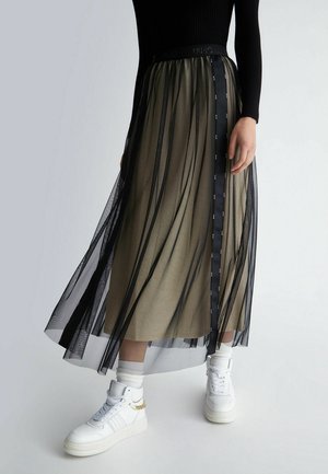 Przezroczysta czarna warstwowa spódnica z metaliczną oliwkową bazą, z czarnym paskiem w talii i wstążką z logo. Połączona z białymi wysokimi trampkami.