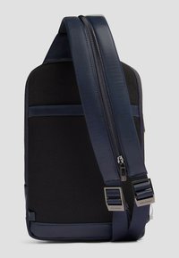 Bolso azul marino con una parte trasera de malla negra texturizada, que cuenta con cierre de cremallera, correa ajustable con herrajes metálicos y un diseño elegante y moderno.