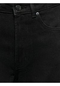 Gros plan sur l'avant d'un jean en denim noir montrant les détails du bouton, de la zone de la fermeture éclair et des coutures de la poche.