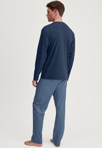 Marineblauwe pyjama-top met lange mouwen, gecombineerd met blauw gemusterde broek met kleine vierkantjes. Lichtgewicht stof, ontspannen pasvorm, ademende textuur.
