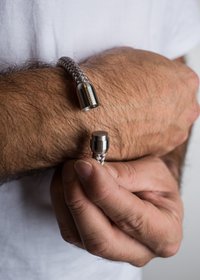 Audimas apyrankė, pagaminta iš pilkos ir smėlio spalvos medžiagos su metaliniais galiniais dangteliais, pasižyminti lygiu paviršiumi ir cilindrine forma.