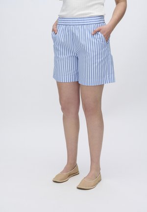 Pantaloni corti a righe blu e bianche con vita elasticizzata e tasche laterali, realizzati in tessuto leggero. Indossati con scarpe beige senza lacci.