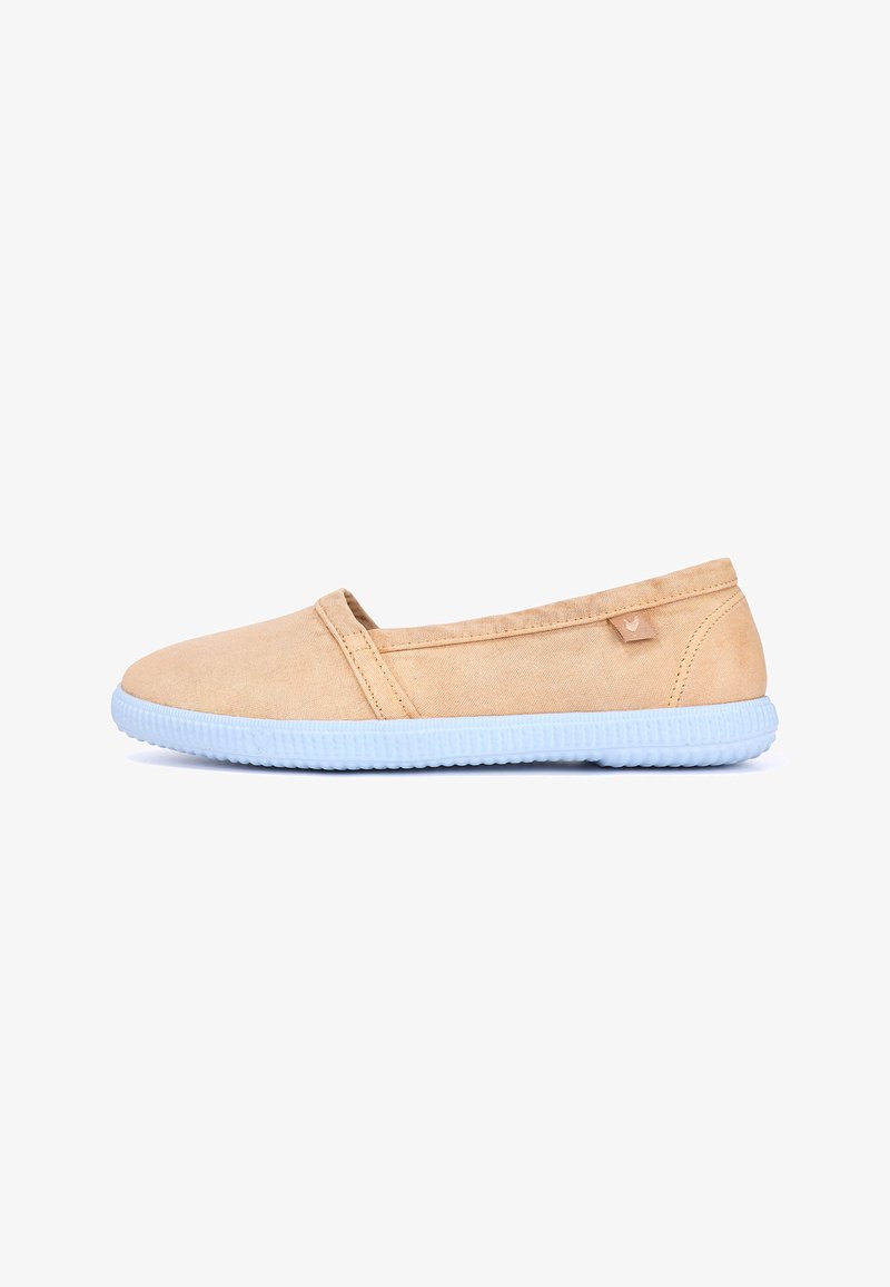 Chaussure décontractée beige à enfiler avec une semelle en caoutchouc texturée blanche, une tige en tissu, et une petite étiquette cousue près du talon.