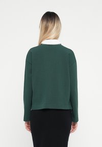 Grön sweatshirt med vit krage, avslappnad passform, långa ärmar och rak nederkant. Mjuk textur utan synliga mönster eller detaljer.