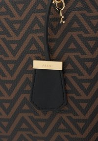 Czarna i brązowa torebka w geometryczny wzór z teksturowym wykończeniem, z ozdobnym zawieszką w kolorze złotym i akcentem w kształcie klucza.