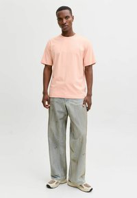 Roosa lühikeste varrukatega puuvillane T-särk ümmarguse kaelusega, kantud heledate hallide, lõtvade teksapükste ja beežide tossudega.