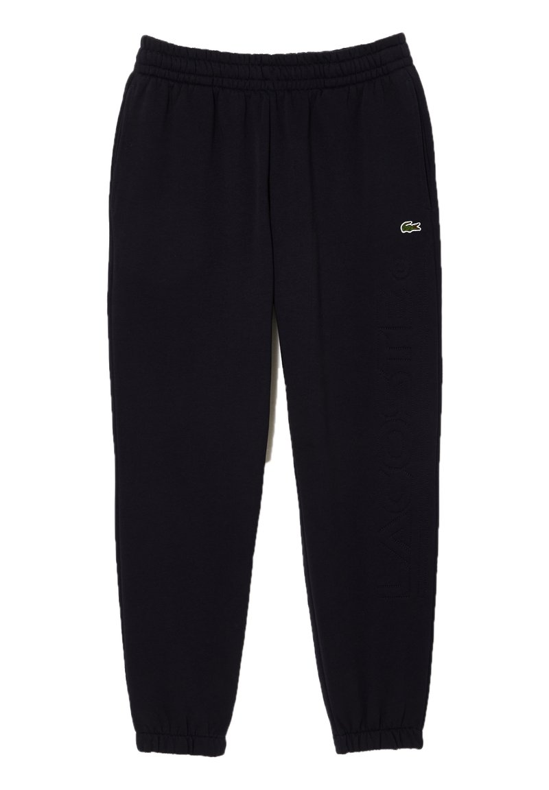 Svarta sweatpants med elastisk midja och smalnade ankelslut. Har en liten grön Lacoste-logotyp och texturerad skrift på sidan.