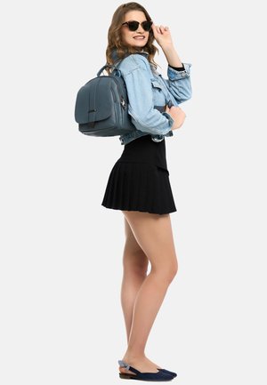 Turdyr grøn læderrygsæk med en frontklap, sølvhardware og dobbelt topgreb, parret med en denimjakke og en sort plisseret nederdel.