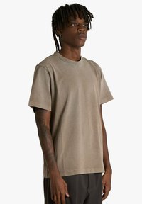 T-shirt di cotone marrone con scollo tondo classico, maniche corte e vestibilità comoda. Texture liscia senza motivi o disegni visibili.