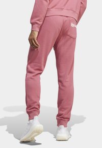 Rosa Jogginghose aus einer softem Baumwollmischung, mit elastischen Bündchen, einer Gesäßtasche und einem Logo auf der rechten Seite. Kombiniert mit weißen Sportschuhen.