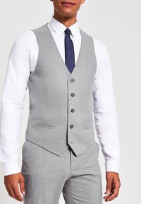 Hellgraue Weste aus strukturiertem Stoff, mit tailliertem Schnitt, fünf Knöpfen und zwei Vorderaschen, kombiniert mit einem weißen Hemd und einer marineblauen Krawatte.