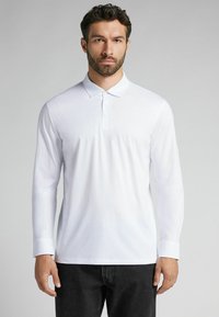 Vit långärmad polo skjorta i bomull. Klassisk krage med tre knappar, figursydd design och manschetter som sträcker sig till handlederna. Svarta jeans.