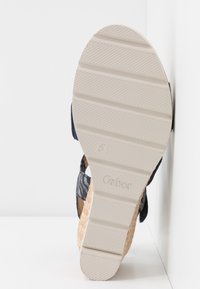 Sandale compensée avec une plateforme en jute texturé, marron clair. La bride de cheville est navy avec un motif floral et une semelle en caoutchouc blanche pour plus d'adhérence.