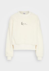 Krémově zbarvená krátká mikina vyrobená z texturované fleecové látky. Má žebrovaný výstřih a manžety s malým vyšitým logem na hrudi.