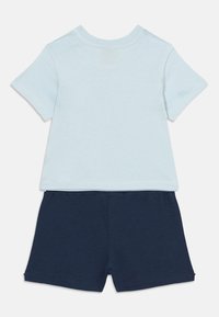 Φωτεινό γαλάζι ο κοντομάνικο μπλουζάκι για νήπια, σε συνδυασμό με σκούρο μπλε σορτς με ελαστική μέση, τοποθετημένα επίπεδα σε λευκό φόντο.