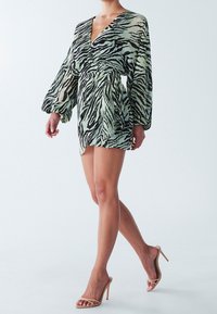 Seeprakuosinen minihamepuku läpikuultavasta, kevyestä kankaasta. Siinä on pitkät puhvikädet, syvä v-kaula-aukko ja vyötärö korostettu muodon esille tuomiseksi.