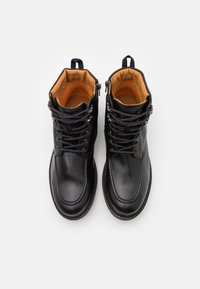 Stivali stringati in pelle nera con rivestimento interno arancione imbottito e linguette per il pollice, visti dall'alto su uno sfondo bianco.