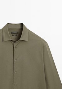 Chemise kaki à manches longues à boutons avec col classique, en coton élasthanne, présentée à plat sur fond blanc.