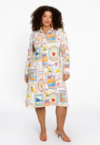 Langärmliges Hemdkleid mit einem bunten, tropischen Druck und sechseckigen Bildern, aus weißem Stoff mit leuchtenden Akzenten und einem Kragen.