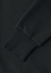 Gros plan sur la manche d’un sweat-shirt noir avec un poignet côtelé et élastique et une texture de tissu lisse.