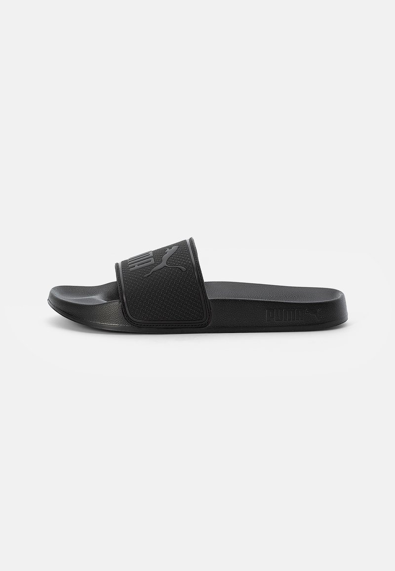 Sandale noire à glissière avec une sangle texturée portant le logo Puma, semelle plate en caoutchouc et design épuré pour une utilisation décontractée.