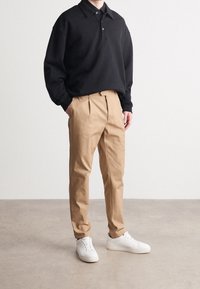 Černé polokošile s dlouhým rukávem, límečkem a knoflíky, doplněné světle hnědými plisovanými kalhotami a bílými teniskami. Jednoduchý, čistý design.