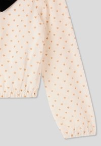 Blusa rosa pesca chiaro con motivo a cuori metallici dorati, polsini arricciati e un tessuto morbido e trasparente. Presenta un colletto in velluto nero.