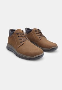 Botine din piele maro la gleznă, cu o textură netedă, detalii contrastante negre la guler și vârf rotund. Au închidere cu șireturi și talpă din cauciuc.