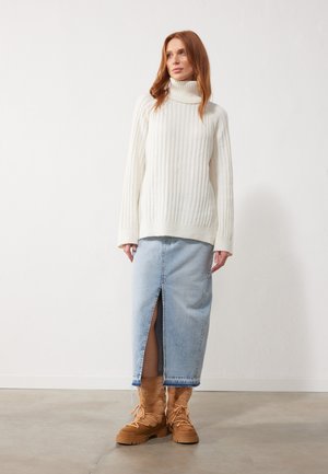 Jersey de cuello alto de canalé crema, falda de mezclilla hasta la rodilla con abertura frontal y botas marrones con cordones y detalles de piel texturizada.