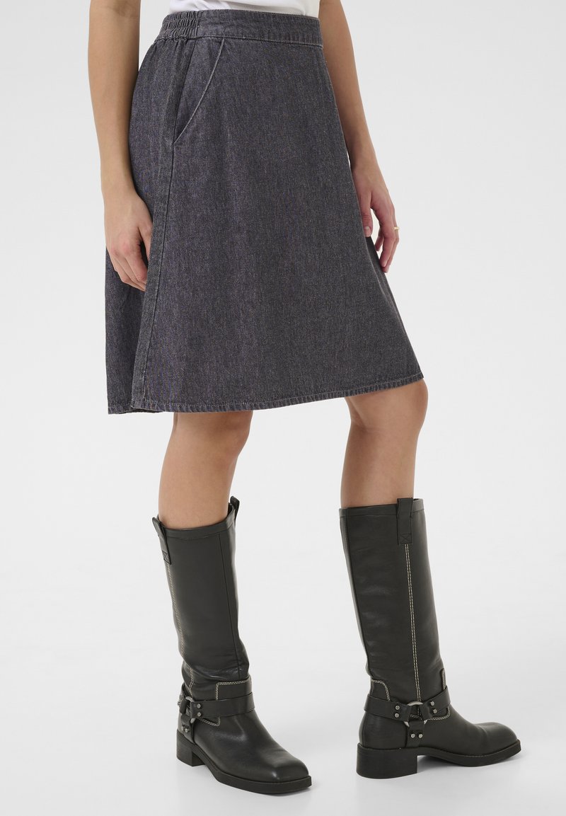 Falda de mezclilla gris hasta la rodilla con bolsillos laterales y cintura elástica, combinada con botas de piel negras hasta la rodilla con hebillas.