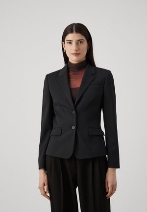 Black tailored blazer with notched lapels, front pockets, two-button closure, and structured fit, worn over a translucent burgundy top.