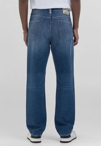 Jean en denim bleu à coupe décontractée, avec une texture délavée, deux poches arrière et un patch de marque sur la ceinture.
